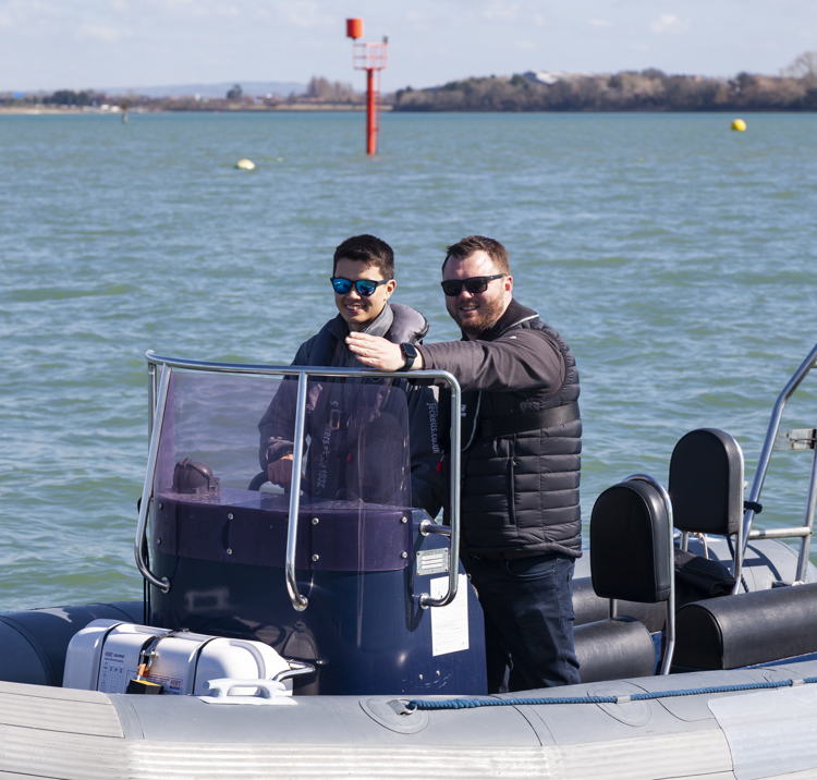 Two men standing on a powerboat, the younger man is steering and older ma is instructing