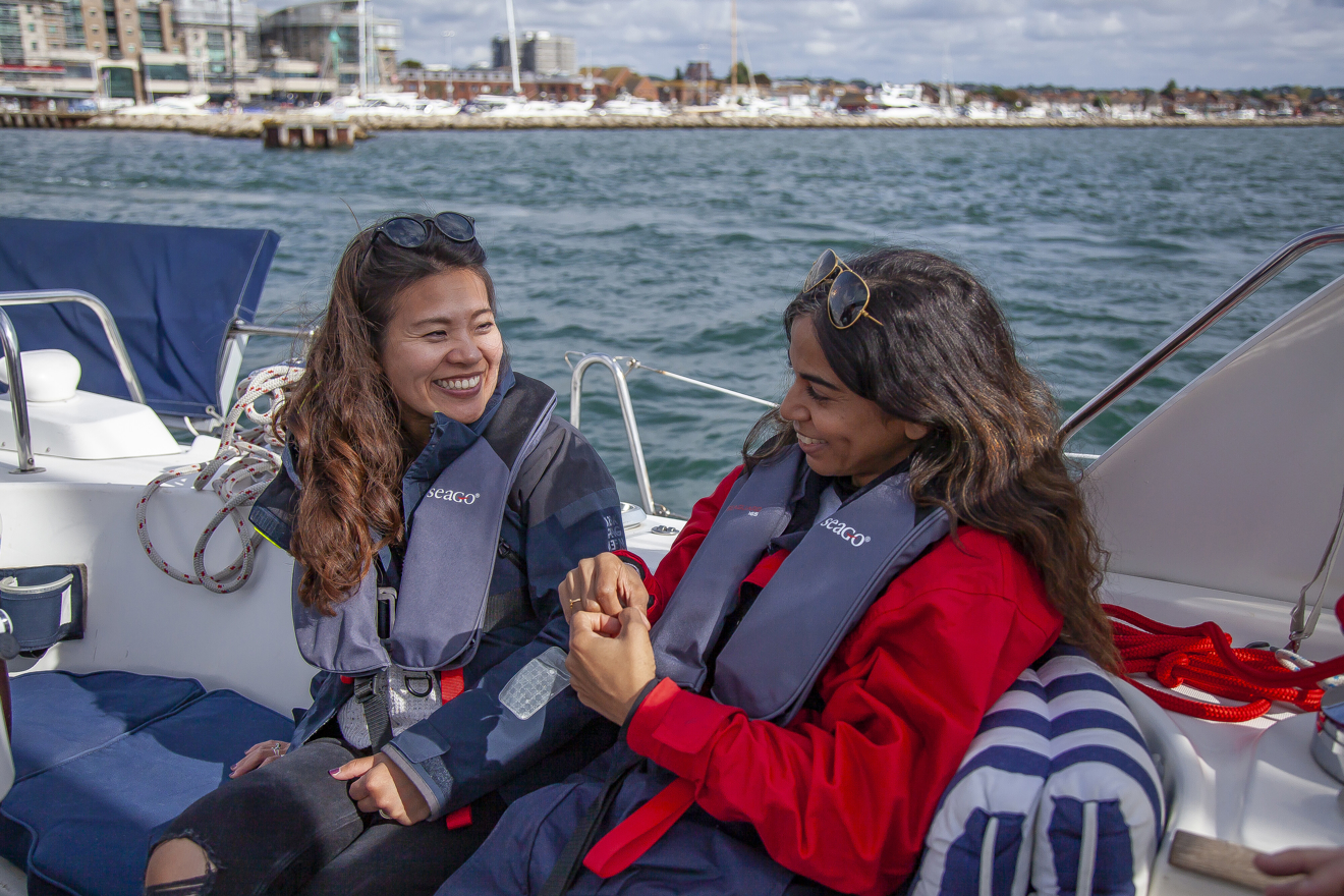 two women sat together on a yacht talking and smiling
