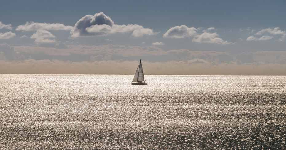 A single boat floating along the horizon at sunset