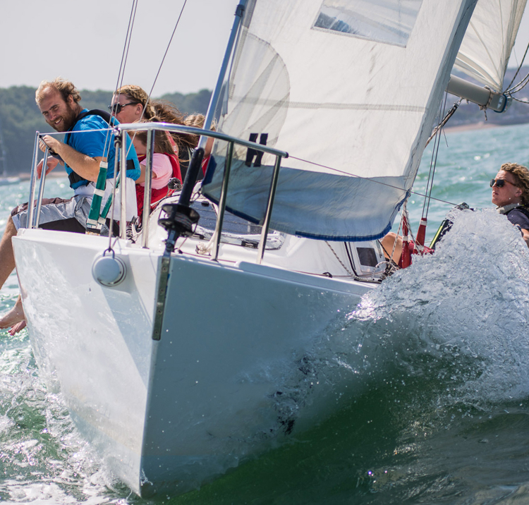 Happy sailors sat on the edge of their sail boat on sunny day
