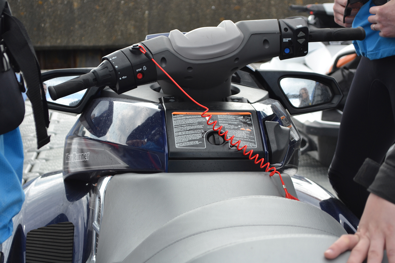 A close-up view of a jet ski dashboard with a safety cord attached, surrounded by people in blue jackets.