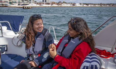 two women sitting on a large yacht smiling at each other