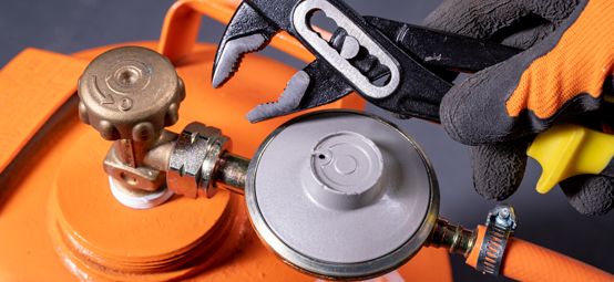 	An image of orange Gas cylinder with a person holding one of the tools to fix the nasal of cylinder