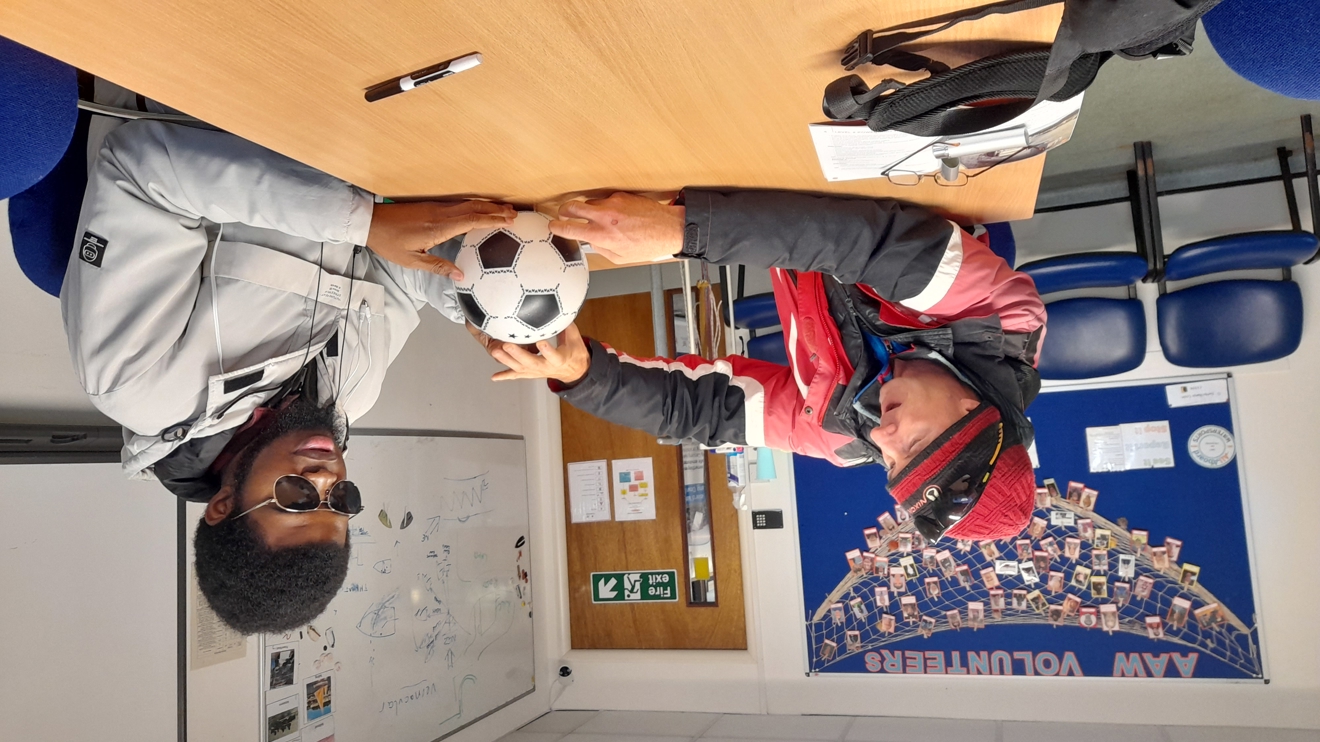 instructor demonstrating something to young man using a football as a an educational prop