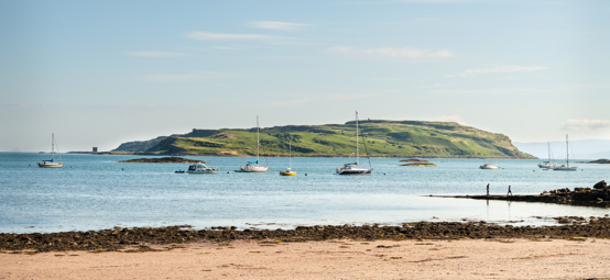 People on the beach in Millport with boats moored in Millport bay, Cumbrae, Scotland