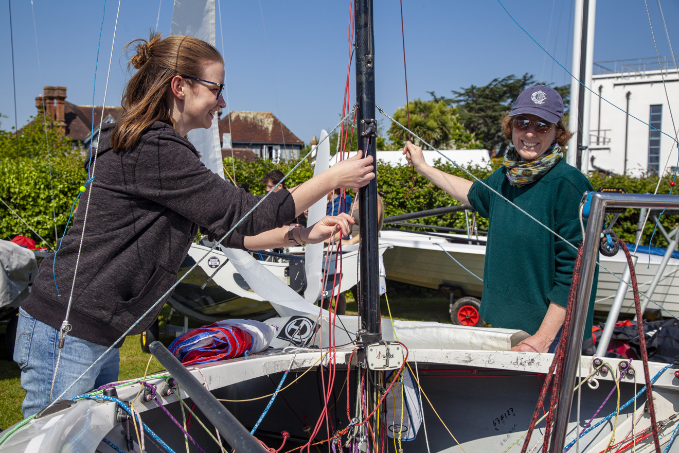 	Two ladies help each other rig a boat in the dinghy park with smiles on their faces