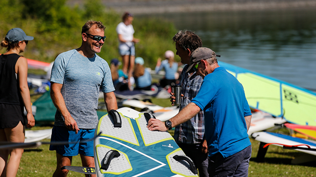 3 men standing around paddle board talking