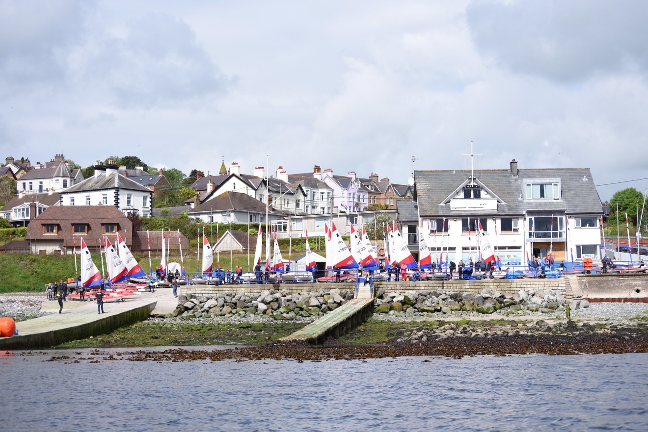 view from the ocean of a sailing club with numerous dinghies  infront of it on shore