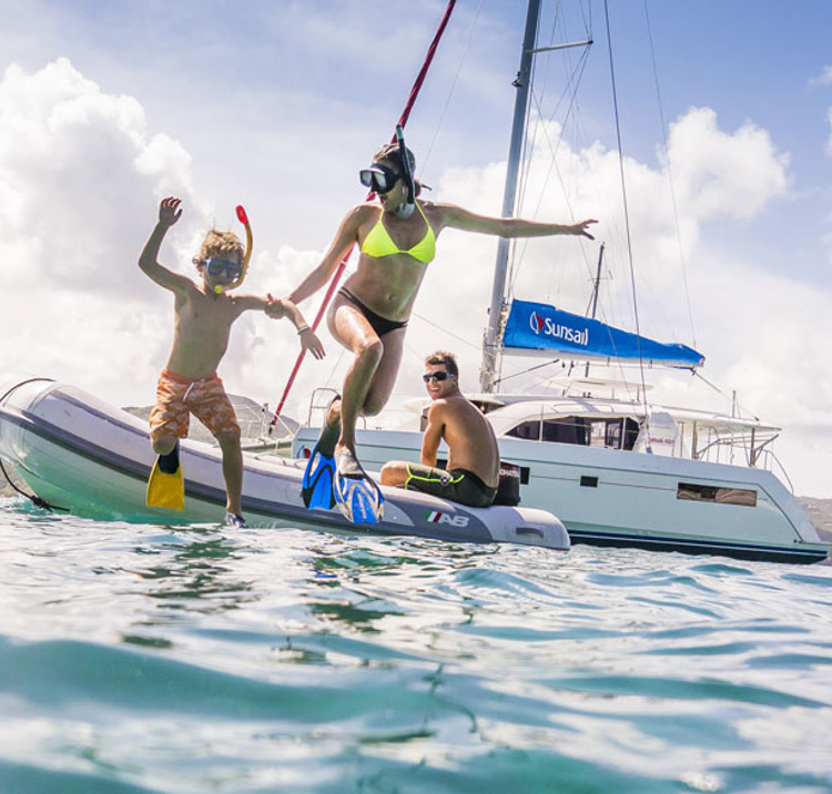 family jumping from dinghy into sea with snorkelling gear and sunsail yacht behind them