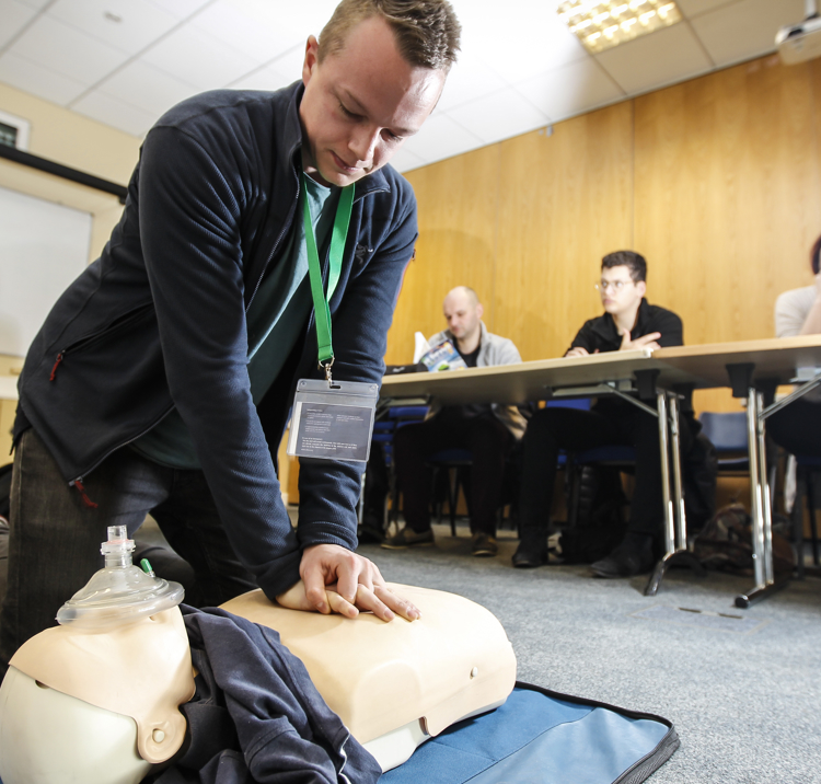 Numerous people in a classroom at a First aid course, one man in knelt on the floor demonstrating CPR on a dummy